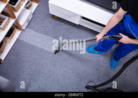 Nahaufnahme eines männlichen Hausmeister mit Staubsauger für den Teppich Reinigung im Wohnzimmer Stockfoto