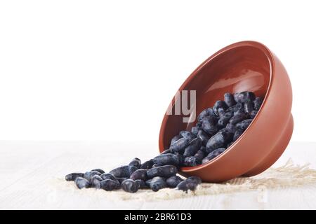 Geißblatt Beeren in einer Keramikschale auf einem Holztisch auf weißem Hintergrund. Stockfoto