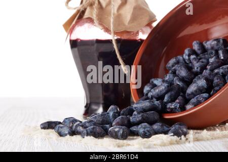 Geißblatt Beeren in einer Keramikschale und Glas Marmelade stehen auf einem Holztisch auf weißem Hintergrund. Stockfoto