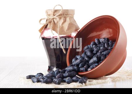 Geißblatt Beeren in einer Keramikschale und Glas Marmelade stehen auf einem Holztisch auf weißem Hintergrund. Stockfoto