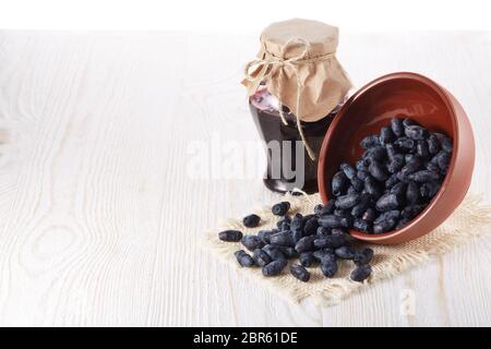 Geißblatt Beeren in einer Keramikschale und Glas Marmelade stehen auf einem hölzernen Hintergrund. Stockfoto