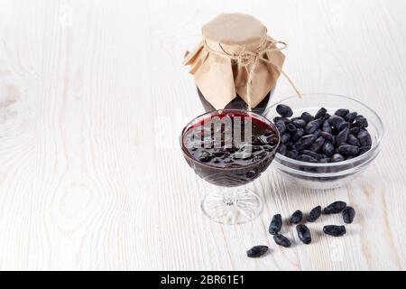 Geißblatt Beeren in einer Glasschüssel und Glas Marmelade stehen auf einem hölzernen Hintergrund. Stockfoto