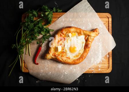 Traditionelles georgisches Gericht chachapuri ajarian im schwarzen Hintergrund. Frisch Gebackener Khachapuri. Georgische Nationalgebäck mit Käse und rohen Eiern Stockfoto