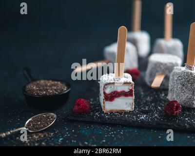 Hausgemachte raw lamington Eis erscheint auf dunklem Hintergrund. Australische süße Nachspeise lamington mit Chia und Himbeeren Marmelade, Schokolade und Kakao. Stockfoto