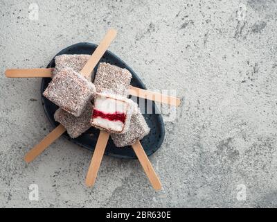 Hausgemachte raw lamington Eis springt auf grauem Hintergrund. Australische süße Nachspeise lamington mit Chia und Himbeeren Marmelade, Schokolade und Kakao. Stockfoto