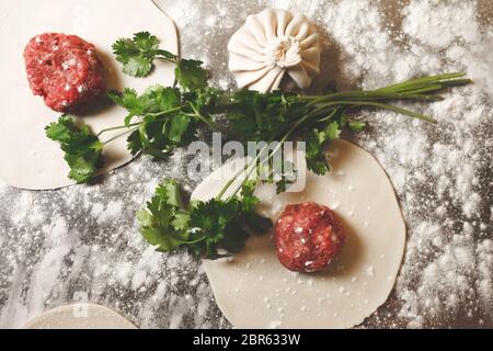 Khinkali Kochprozess. Georgische nationale Küche Konzept. Khinkali, Teig, Koriander und Fleischfüllung auf einem Tisch ausgelegt Stockfoto