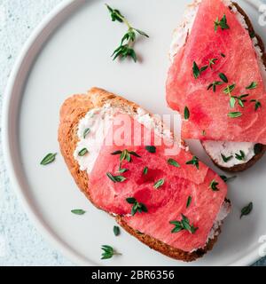 Toast mit Frischkäse und Wassermelone. Salzige käse, süßes Wassermelone und würziger Thymian auf knusprig gegrillte Brotscheiben. Idee und Rezept ungewöhnliche Gesunde br Stockfoto