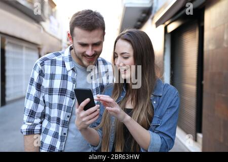 Vorderansicht von zwei Freunden surfen smart phone Inhalt zu Fuß auf der Straße Stockfoto