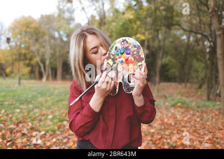 Junge Malerin mischt Farben auf einer Palette, die sie in den Händen hält. Stockfoto