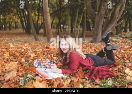 Der junge Künstler liegt im Herbstpark auf einem Plaid und malt ein Bild. Mädchen zeichnet ein Bild im Park Stockfoto