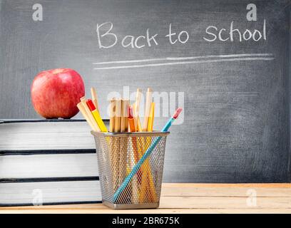 Stapel Bücher mit Apple und Bleistifte in Korb Behälter auf hölzernen Tisch und Tafel mit Zurück in die Schule. Zurück zu Schule Konzept Stockfoto