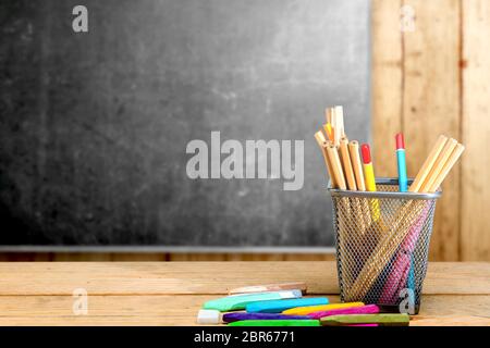 Bleistifte in Korb Behälter und bunte Wachsmalkreiden auf dem hölzernen Tisch mit blackboard Hintergrund. Zurück zu Schule Konzept Stockfoto