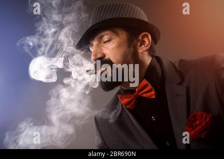 Eleganter Gentleman in Anzug, Fliege und Hut genießt in Rauchen hochwertige Zigarre. Stockfoto
