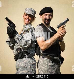 Die lächelnden weiblichen und männlichen Soldaten in Militäruniform posieren mit Pistolen in den Händen. Stockfoto