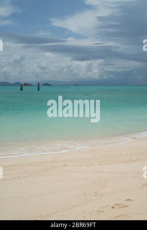 Blick vom Strand auf Holzpfählen in kristallklarem Meerwasser über Boote und bewölktem Himmel Hintergrund Stockfoto