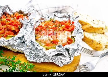 Rosa Lachs mit Zucchini, Tomaten, Zwiebeln, Knoblauch und Thymian, in Folie gebacken, Gabel und Brot auf einem Holzbrett Hintergrund Stockfoto