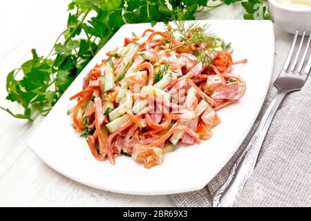 Aus geräucherter Wurst Salat, pikant Karotte, Tomate, Gurke und Gewürze, gekleidet mit Mayonnaise, Handtuch, Gabel und Petersilie vor dem Hintergrund der lig Stockfoto