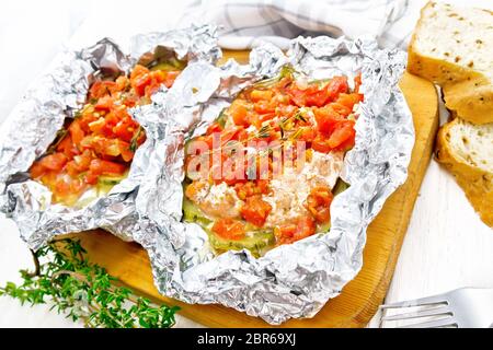 Rosa Lachs mit Zucchini, Tomaten, Zwiebeln, Knoblauch und Thymian, in Folie gebacken, Gabel und Brot auf ein weißes Holzbrett Hintergrund Stockfoto