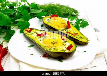 Rührei mit Peperoni in zwei Hälften von Avocado in eine Platte auf Serviette, Gabel, Petersilie auf einem Holzbrett Hintergrund Stockfoto