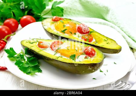 Rührei mit Tomaten in zwei Hälften von Avocado in einer Platte, Handtuch und Gabel auf dem Hintergrund der Holzbretter Stockfoto