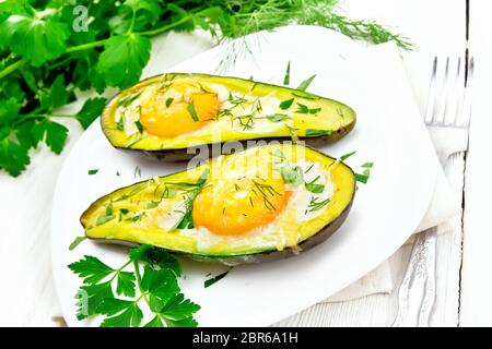 Rührei mit würzigen Grünen in zwei Hälften von Avocado in eine Platte auf dem Handtuch, Gabel, Petersilie auf Holzbrett Hintergrund Stockfoto