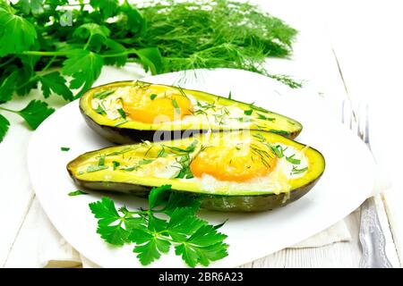 Rührei mit würzigen Grünen in zwei Hälften von Avocado in eine Platte auf dem Handtuch, Gabel, Petersilie auf dem Hintergrund der hellen Holzmöbeln board Stockfoto