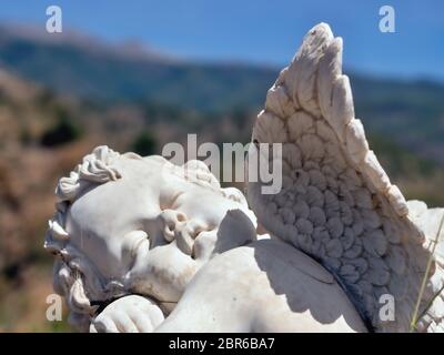 Ein Engel im Garten zwischen den Blumen mit Vorderansicht, der eine Flügel sichtbar ist, wird der Kopf gedreht wird, kindliche Gesicht einschlafen, in der Nähe Stockfoto