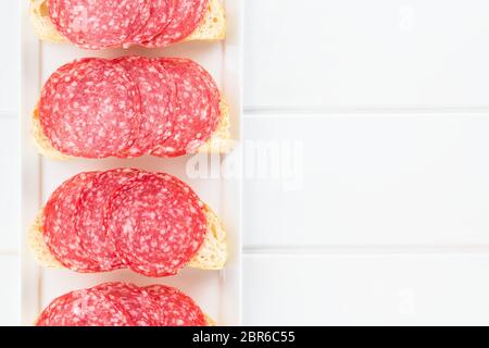 Salamischeiben auf ciabatta Brot, Overhead, fotografiert auf weißem Holz (selektive Fokus, Fokus auf der Salami Scheiben) Stockfoto