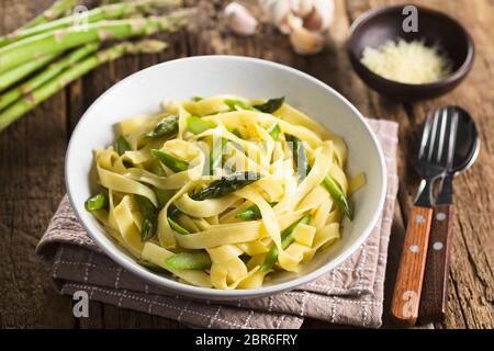 Frische, hausgemachte Pasta Teller Fettuccine oder Tagliatelle, grün Spargel, Knoblauch und Zitronensaft in der Schüssel, Zutaten und geriebenen Käse in der Rückseite (Se Stockfoto