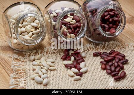 Verschiedene Arten von trockenen Harikots in Glasgefäßen liegen auf Holzhintergrund. Verschiedene Arten Hülsenfrüchte. Stockfoto