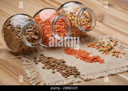 Verschiedene Arten von trockenen Linsen in Glasgefäßen liegen auf Holzhintergrund. Verschiedene Arten Hülsenfrüchte. Stockfoto