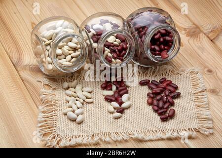 Verschiedene Arten von trockenen Harikots in Glasgefäßen liegen auf Holzhintergrund. Verschiedene Arten Hülsenfrüchte. Stockfoto