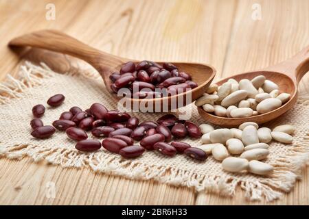 Verschiedene Arten von trockenen Harikots auf Holzlöffeln liegen auf Holzhintergrund. Verschiedene Arten Hülsenfrüchte. Stockfoto