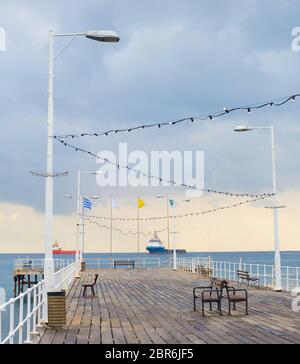 Hölzerne Seebrücke in Limassol Promenade. Indusrtial Frachtschiffe im Hintergrund. Zypern Stockfoto