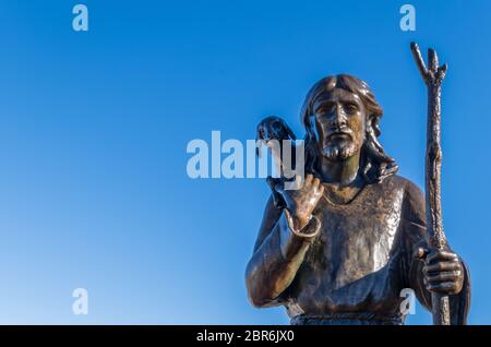 Antike Bronzestatue von Jesus Christus, dem Guten Hirten, der das verlorene Schaf auf seine Schultern, auf blauem Himmel Hintergrund isoliert. Platz für Text. Stockfoto