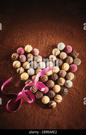 Herz förmige Anordnung von Luxus hand aus kugelförmigen Pralinen auf einem Bett von Kakaopulver mit einem Twirled Pink Ribbon für einen Schatz am Valentines d Stockfoto