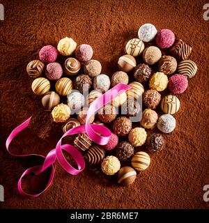 Romantische Herz förmige Anordnung von Schokolade Bonbons mit einem Twirled Pink Ribbon auf einem Hintergrund von Kakaopulver in Nahaufnahme quadratischen Format für Valenti Stockfoto