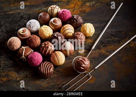 Handgemachte Schokolade praline Praline Display mit einer ordentlichen Rechteck der sortierten Fondant auf rustikalem Holz mit Draht Heber und Gabel Stockfoto