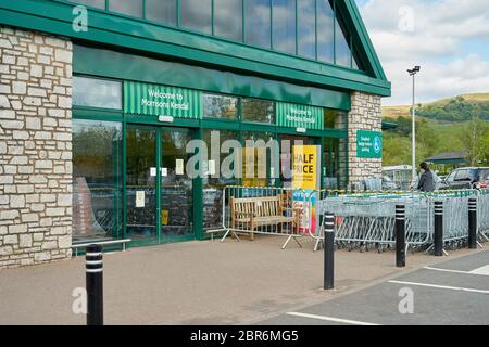 Grüne Fassade des Eingangs zum Morrisons Supermarkt mit Barrieren, die Käufer über ein Einbahnsystem in den Laden leiten, aufgrund von Covid 19, Coronavirus Stockfoto