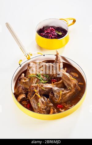 Roast wilde Kaninchen Wild in einem reichhaltigen Soße überbacken mit frischen Kräutern, Orangenschale und Pilze in einem gelben Emaille serviert pan mit Beilage der Roten cabba Stockfoto