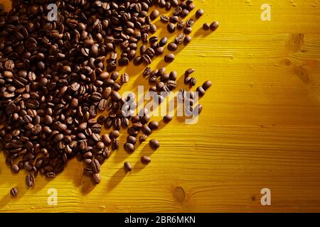 Gestreute geröstete Kaffeebohnen auf Gelb gebeizt in der oberen linken Ecke angeordnet mit seitlichen Platz kopieren Stockfoto