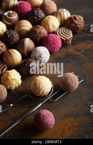 Auswahl von luxuriösen Schokolade Fondant- oder Pralinen auf rustikalem Holz mit Schokolade überzogen, weiße und rote Kugeln auf einem vintage Kabel Gabel und Li angezeigt Stockfoto