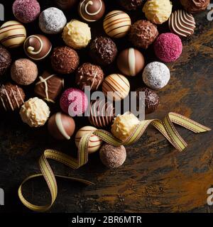 Elegante Werbung Anzeige von Gourmet hausgemachte Pralinen und Schokoladen auf ein rustikales Holz Hintergrund mit wirbelnden gold Farbband im quadratischen Format Stockfoto