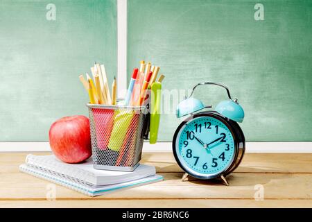 Stapel von Notebooks mit Apple und Bleistifte in Korb Container mit grünen Hefter und Wecker auf dem Holztisch mit schiefertafel Hintergrund. Back t Stockfoto