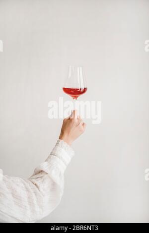 Frauen Hand hält Glas Roséwein über weißen Wand Hintergrund. Weinladen, Weinprobe, Bar, Weinkarte Konzept Stockfoto