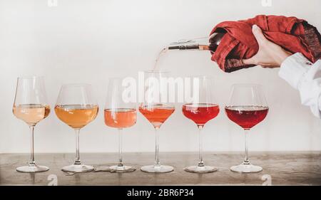 Shades of Rose Wein in stieligen Gläsern in Reihe gestellt und Frauen Hand Gießen Wein aus Flasche zu Glas, weiße Wand Hintergrund dahinter. Weinbar, Wein Stockfoto