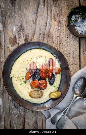 Vegane cremige Polenta mit gerösteten Mossälen auf Holzgrund. Stockfoto