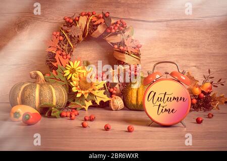 Wecker, Text Herbstzeit. Umweltfreundliche, rustikale Einrichtung ohne Abfall. Herbstblätter, gelbe Blüten, dekorativer Kranz, Herbstblätter und Beeren. Natürlich Stockfoto