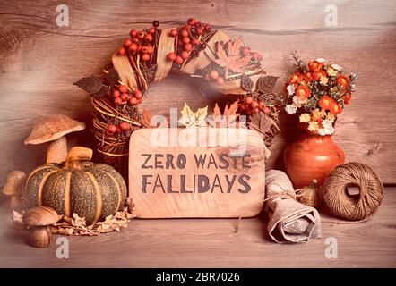 Text 'Zero Waste Fallidays' auf Holzbrett. Traditionelle Herbstdekorationen, getöntes Bild. Herbstkranz mit Beeren, Pilzen, Kürbissen, Blumen auf wo Stockfoto