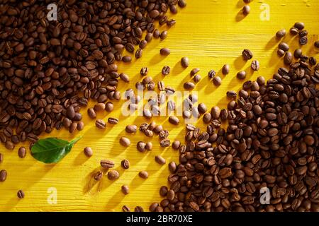 Frisch geröstete Kaffeebohnen in gegenüberliegenden Ecken mit diagonalen Linie zwischen auf gelbem Hintergrund Holz in einer Ansicht von oben Stockfoto